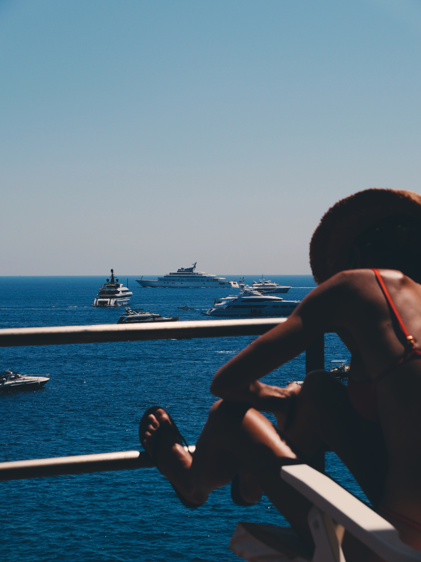 Sunlit harbour view from a balcony, yachts anchored on deep blue water